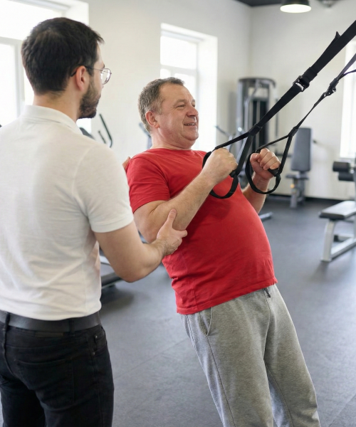 Personal Trainer Wladi unterstützt einen Klienten bei der korrekten Ausführung von TRX-Suspensionstraining in einem Fitnessstudio in Osnabrück.